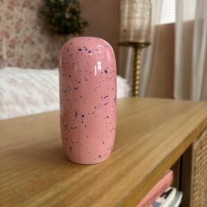 Vaso cilindrico in ceramica rosa con finitura speckled blu, posizionato su un comodino in legno chiaro.