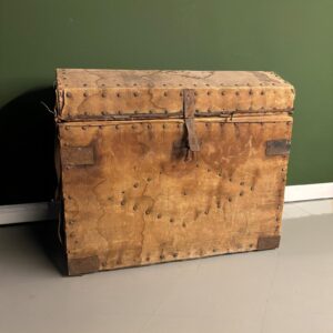 Baule antico da viaggio rivestito in tela beige-marrone con borchie e rinforzi metallici, su sfondo verde.