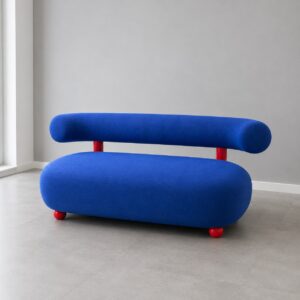 Divano moderno con seduta ovale e schienale cilindrico in tessuto blu, supporti verticali e piedini sferici rossi, su pavimento grigio.