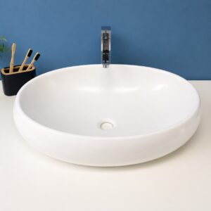 Lavabo da appoggio ovale in ceramica bianca lucida con rubinetto cromato su mobile bianco e parete blu.