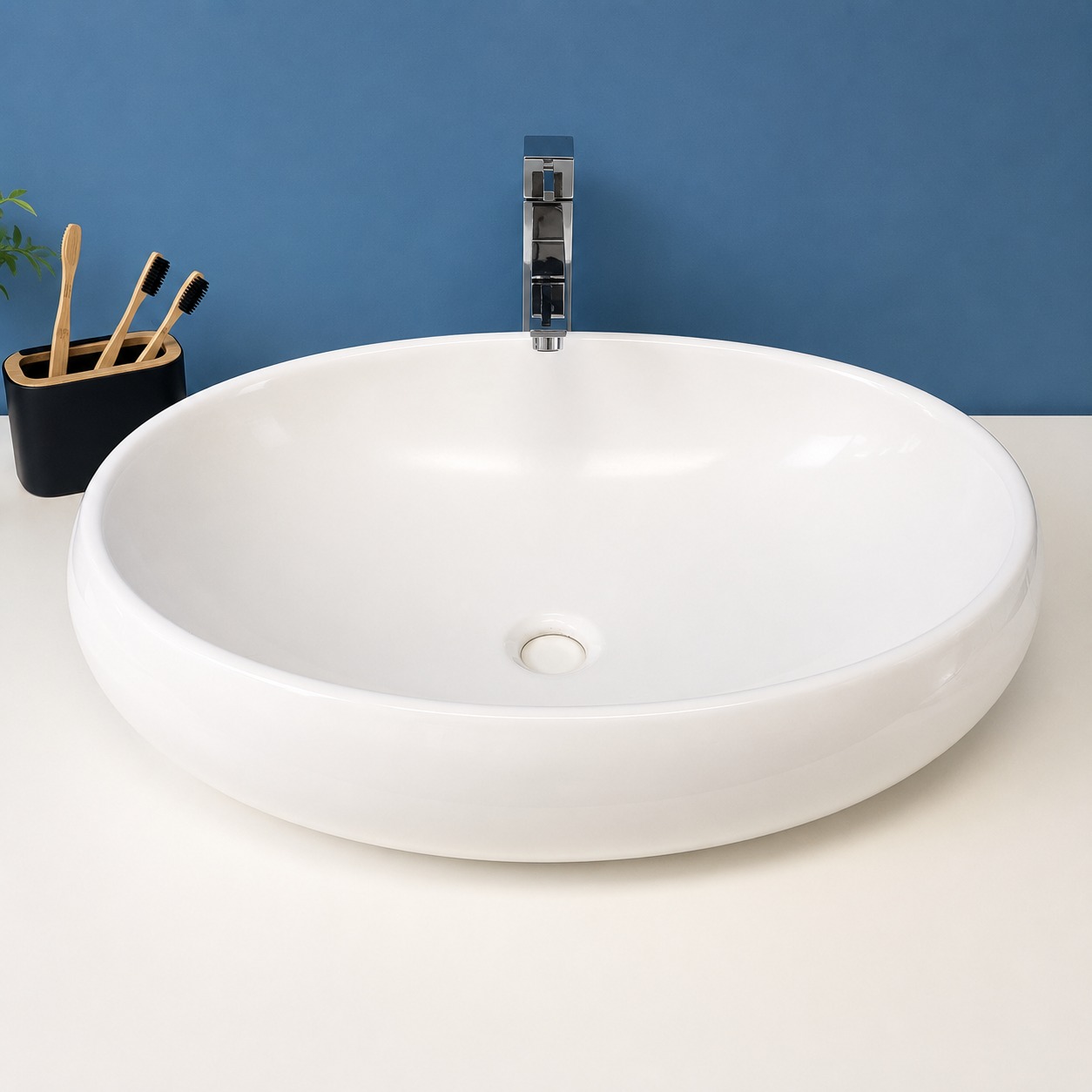 Lavabo da appoggio ovale in ceramica bianca lucida con rubinetto cromato su mobile bianco e parete blu.