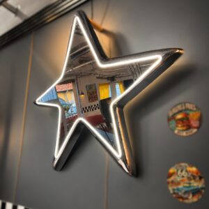 Specchio a forma di stella con cornice cromata e illuminazione LED bianca, riflettente, appeso su parete grigia.