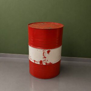 Fusto metallico industriale rosso e bianco con vernice scrostata, posizionato su pavimento grigio davanti a parete verde.