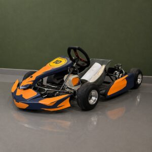 Kart da corsa arancione e blu con numero 10, posizionato su pavimento grigio davanti a una parete verde.
