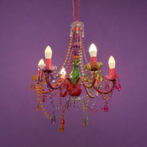 Lampadario eclettico a sei bracci con struttura rossa, decorato con perline e pendenti in vetro e acrilico multicolore su sfondo viola.