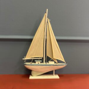 Modello di veliero decorativo in legno con scafo bianco e azzurro, vele beige, su base bianca, contro parete grigia.