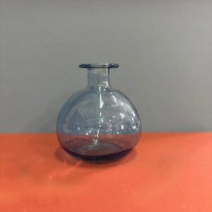 Vaso sferico in vetro soffiato di colore blu-grigio trasparente con collo stretto e orlo svasato, su sfondo arancione e grigio.
