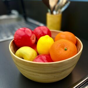 Ciotola in legno chiaro riempita con frutta artificiale realistica: mele rosse e gialle, un limone e mandarini.