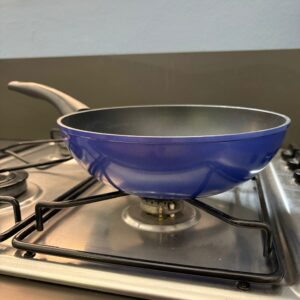 Padella antiaderente blu con manico grigio scuro posizionata su un fornello a gas in acciaio inossidabile.