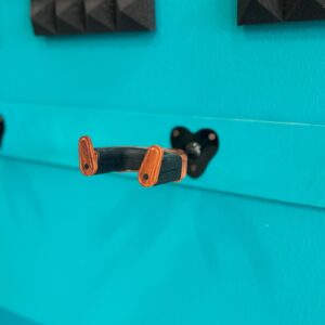 Supporto da parete per strumento musicale con bracci in finitura legno e base nera, montato su una parete turchese.