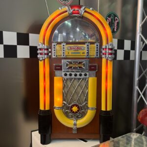 Jukebox decorativo vintage giallo e rosso con dettagli cromati e illuminazione interna, posizionato su sfondo a scacchi.