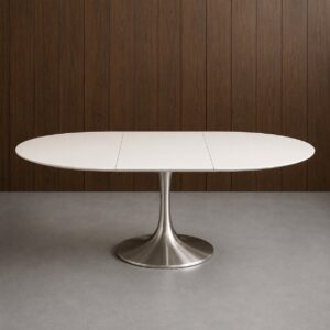 Tavolo ovale allungabile con piano bianco opaco e base a colonna in metallo spazzolato, su pavimento grigio con parete in legno scuro.