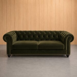 Divano Chesterfield a due posti in velluto verde scuro con bottoni capitonné e borchie decorative, su sfondo in legno chiaro.