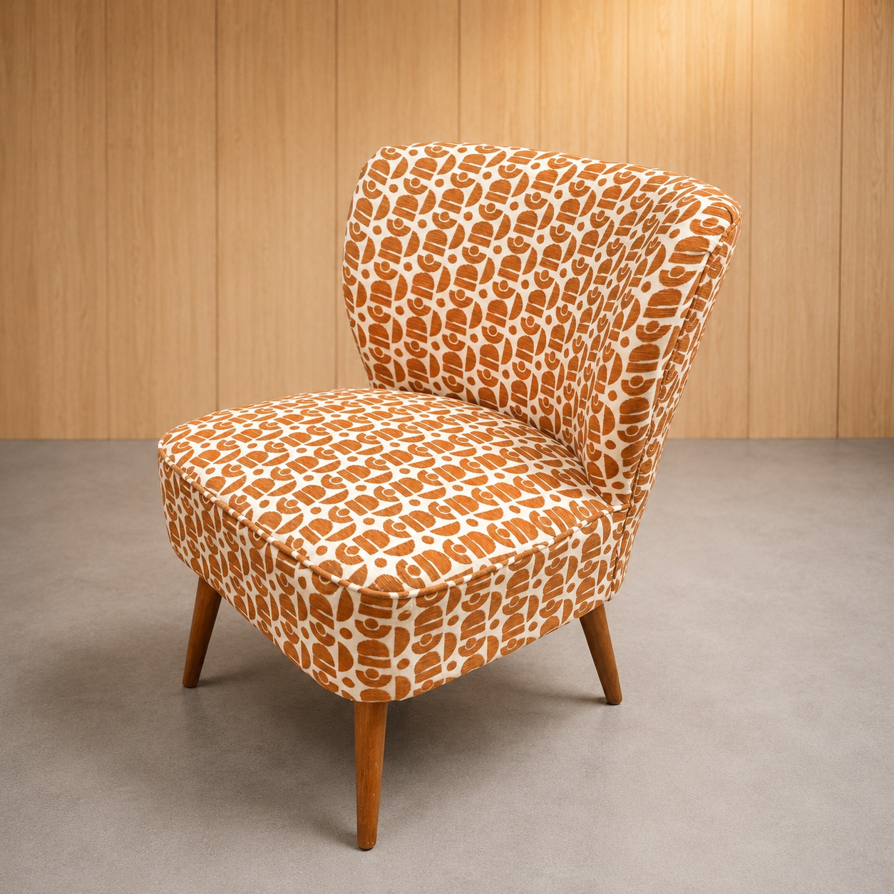 Poltroncina vintage con rivestimento in tessuto a fantasia geometrica arancione e bianca, gambe affusolate in legno chiaro.