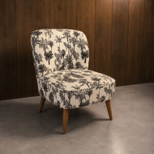 Poltroncina slipper imbottita con tessuto a stampa tropicale bianco e nero (palme e tigri), gambe in legno chiaro, su pavimento grigio e parete in legno scuro.