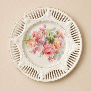 Piatto decorativo rotondo in porcellana bianca con bordo traforato dorato e un bouquet centrale di rose rosa e gialle.