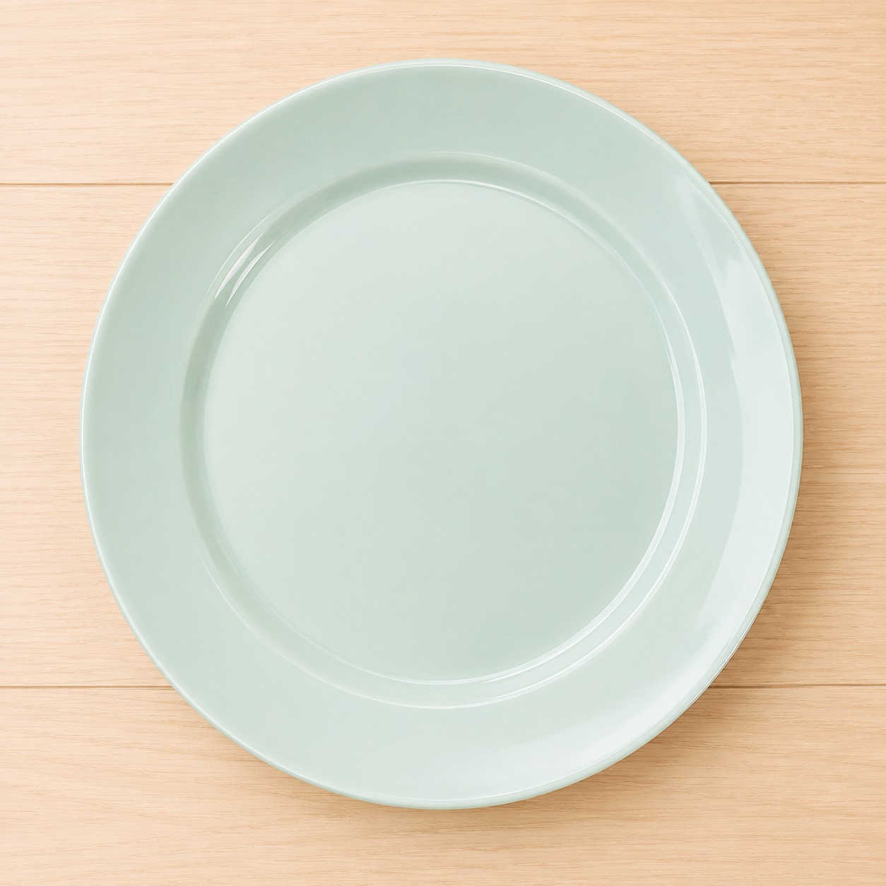 Piatto piano rotondo in ceramica di colore verde acqua, posizionato su una superficie di legno chiaro.