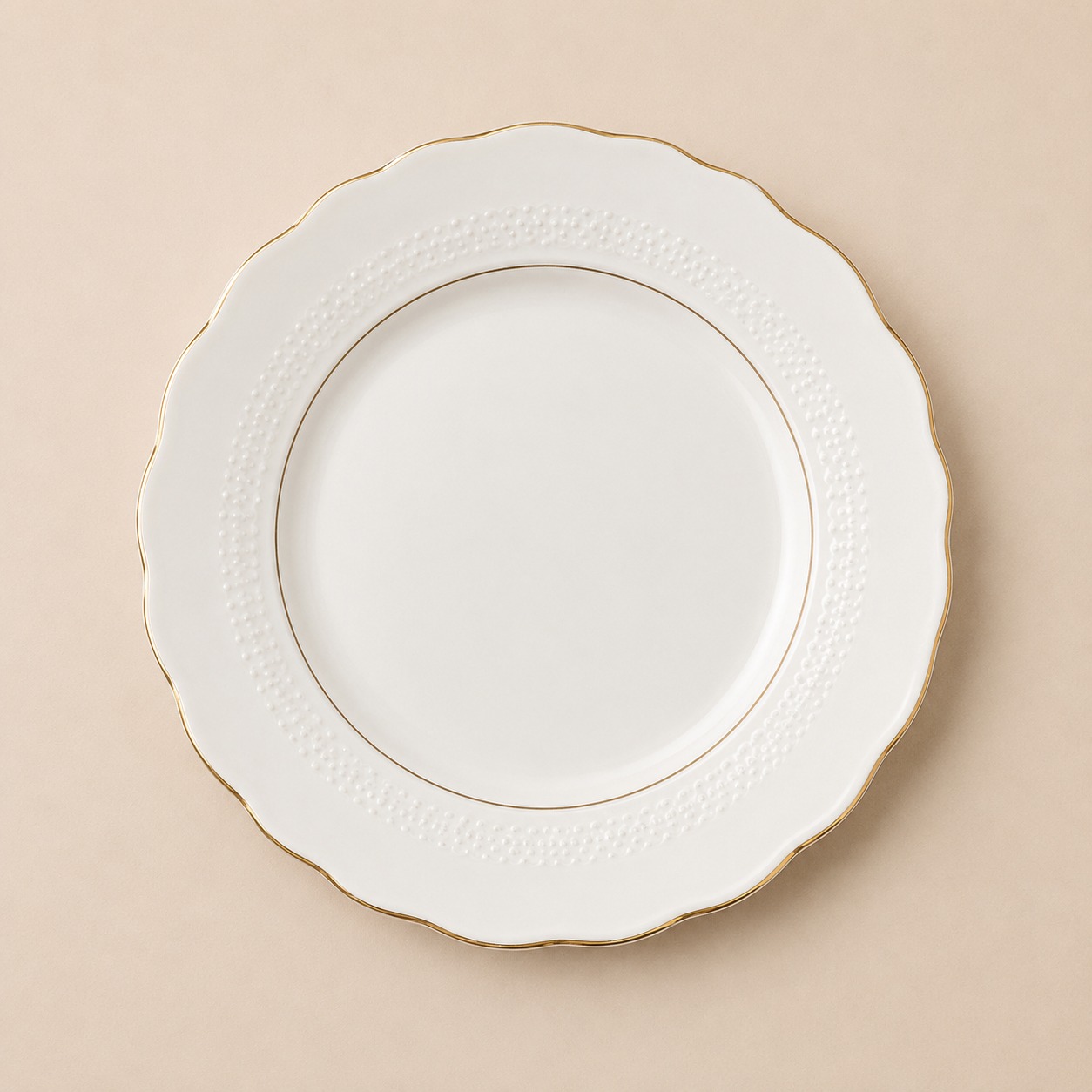 Piatto piano in ceramica bianca con bordo ondulato dorato e motivo a puntini in rilievo, su sfondo beige.