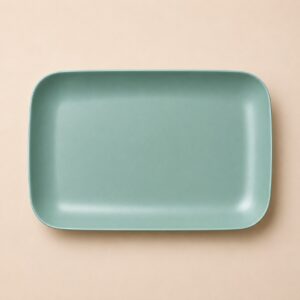 Vassoio rettangolare in ceramica o resina di colore verde acqua opaco, visto dall'alto su sfondo beige chiaro.