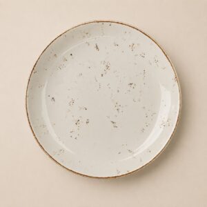 Piatto rotondo in ceramica bianco sporco con finitura smaltata, bordi marroni e macchie rustiche sparse.