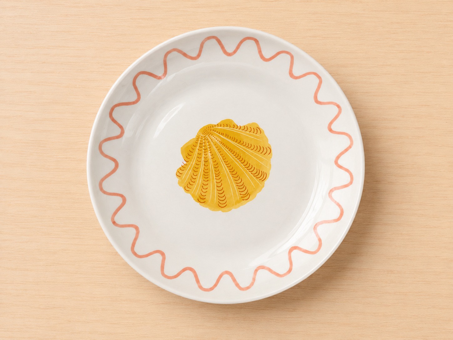 Piatto in ceramica bianca con una conchiglia di capesante gialla al centro e un bordo ondulato rosa su un tavolo di legno chiaro.