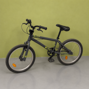 Bicicletta BMX grigia con ruote da 20 pollici e grafiche gialle, posizionata su pavimento grigio davanti a parete verde.