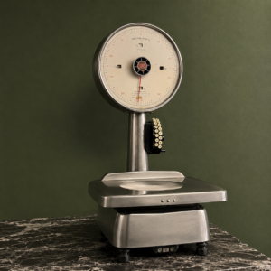 Bilancia meccanica vintage Rheninghaus in metallo spazzolato con ampio quadrante crema e lancetta rossa, su sfondo verde scuro.