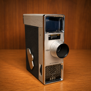Cinepresa Meopta A8G 8mm vintage, colore argento e nero, su sfondo di legno, ideale come oggetto di scena per produzioni.