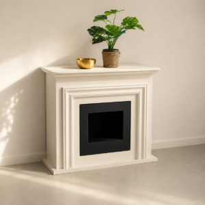 Cornice camino decorativa bianca con inserto nero, posta contro una parete chiara, con una pianta e una ciotola dorata sopra.