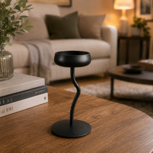 Portacandela singolo in metallo nero opaco con stelo ondulato e base circolare, posizionato su un tavolino in legno.