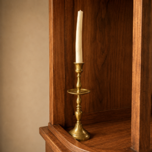 Candelabro in ottone lucido con candela bianca, posizionato su una superficie di legno scuro, evocando un'atmosfera classica.