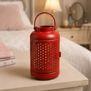 Lanterna decorativa in metallo rosso con finitura invecchiata e design perforato, posizionata su un comodino.