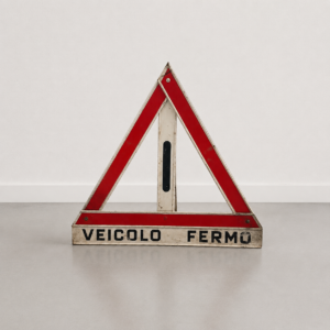 Segnale triangolare di emergenza stradale vintage con scritta "VEICOLO FERMO", struttura in metallo bianco e bande rosse riflettenti, su sfondo neutro.