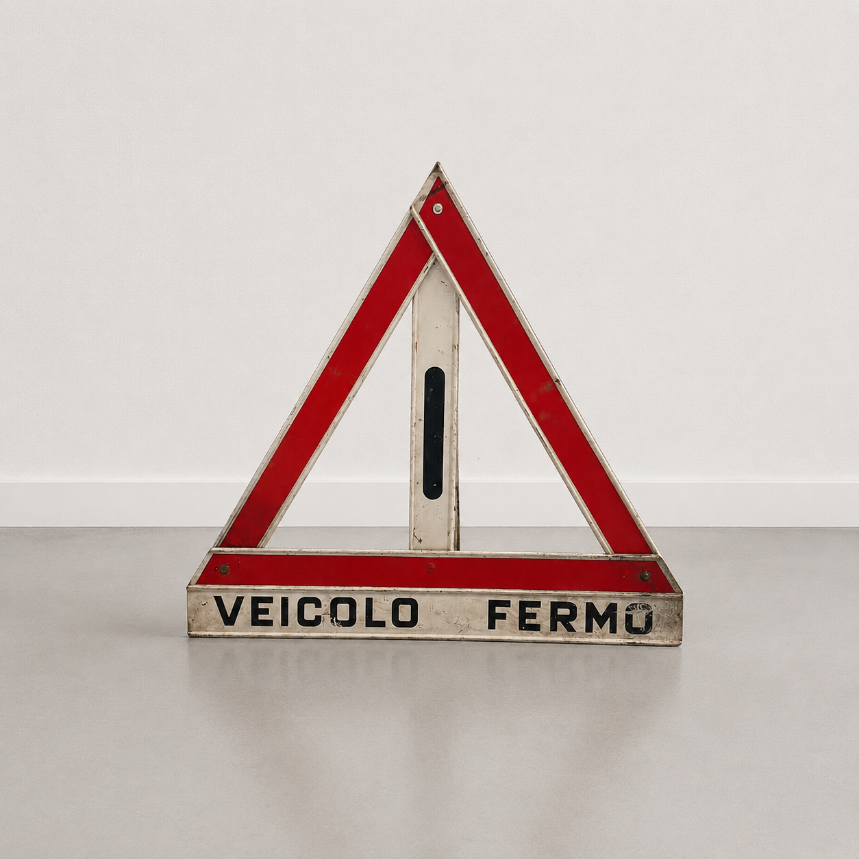 Segnale triangolare di emergenza stradale vintage con scritta "VEICOLO FERMO", struttura in metallo bianco e bande rosse riflettenti, su sfondo neutro.