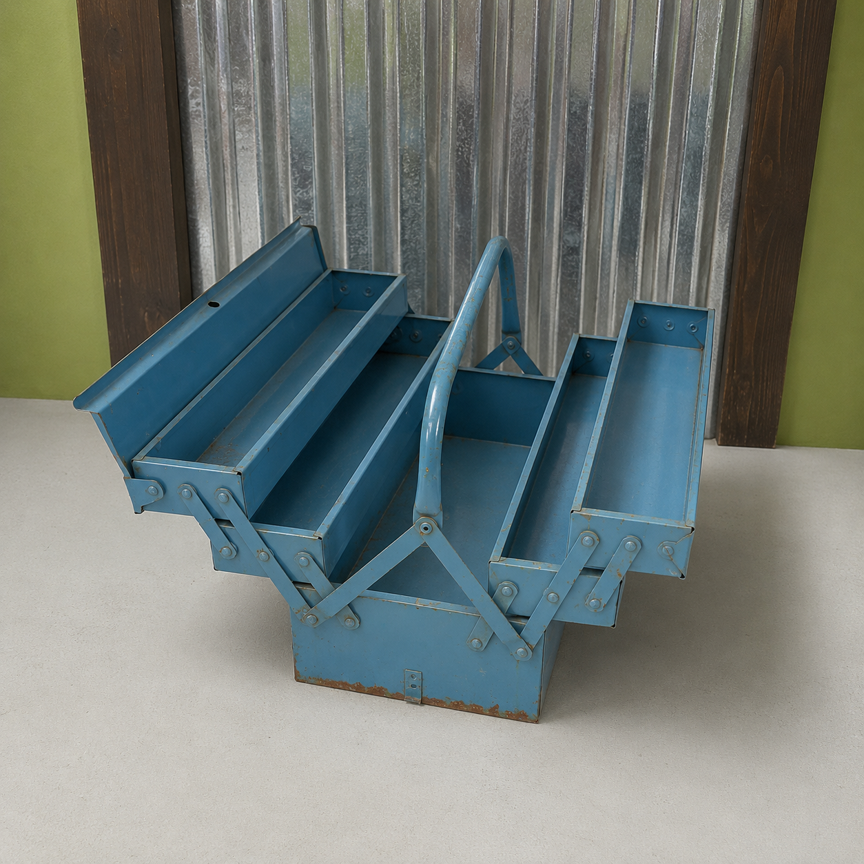 Cassetta degli attrezzi vintage in metallo blu aperta, con scomparti a fisarmonica e segni di usura, su sfondo industriale.