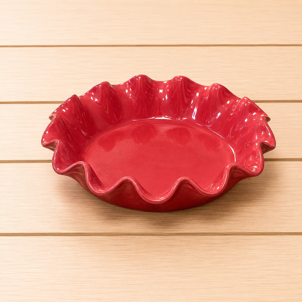 Teglia da torta in ceramica rossa lucida con bordo ondulato, posizionata su un tavolo di legno chiaro.