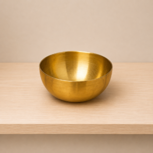 Ciotola decorativa in ottone lucido color oro, posizionata su una superficie di legno chiaro con sfondo neutro.