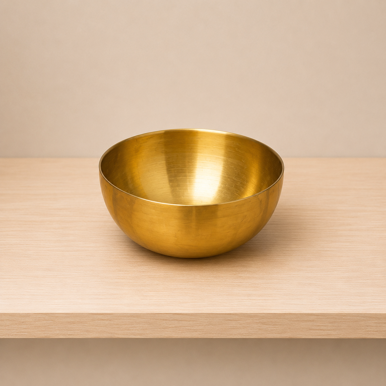 Ciotola decorativa in ottone lucido color oro, posizionata su una superficie di legno chiaro con sfondo neutro.