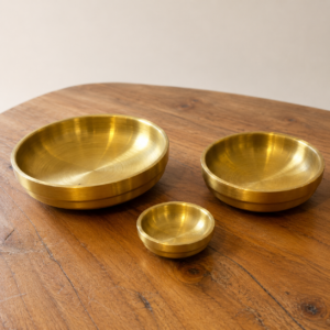 Tre ciotole in ottone massiccio di diverse dimensioni, con finitura spazzolata, posizionate su un tavolo di legno.