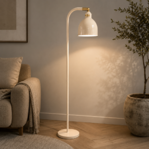 Lampada da terra ad arco color bianco crema con paralume a campana e dettagli in ottone, accesa in un ambiente interno.