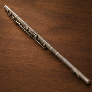 Flauto traverso vintage in metallo argentato con patina scura, posizionato diagonalmente su una superficie di legno scuro.