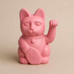 Statuetta di Maneki-neko rosa opaco con zampa alzata e moneta, su sfondo neutro.