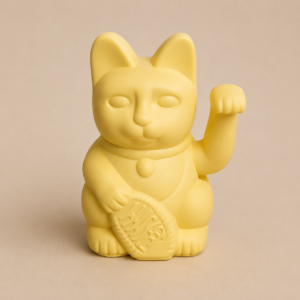 Statuetta di gatto Maneki-neko giallo opaco con zampa alzata e moneta, su sfondo neutro.