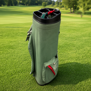 Sacca da golf verde in tessuto con dettagli rossi e neri, posizionata verticalmente su un prato verde di campo da golf.