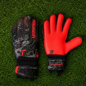 Coppia di guanti da portiere Reusch Prokeeper neri, grigi e rossi su erba sintetica, uno con dorso e uno con palmo visibile.