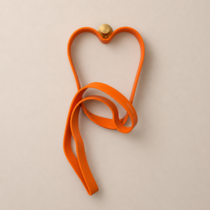 Banda di resistenza arancione brillante a forma di cuore, appesa a un pomello dorato su una parete beige.