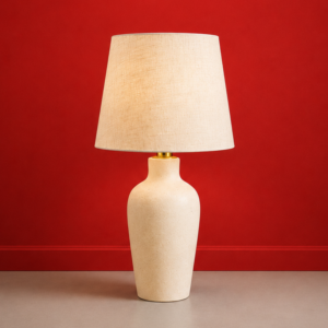 Lampada da tavolo con base in ceramica beige testurizzata e paralume conico in tessuto chiaro, su sfondo rosso.