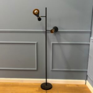 Lampada da terra nera con due diffusori conici orientabili e interni dorati, su sfondo grigio e pavimento in legno.