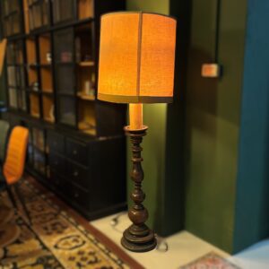 Piantana vintage con fusto in legno scuro tornito e paralume cilindrico in tessuto color ocra acceso, illuminata in un ambiente interno.
