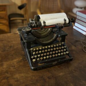 Macchina da scrivere Woodstock No. 5 d'epoca nera su tavolo di legno, con foglio di carta inserito e tasti rotondi.